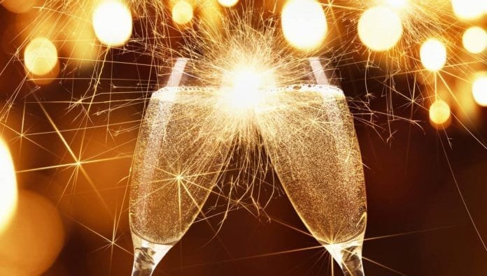 Glasses of champagne and sparklers on bright background with bokeh effect