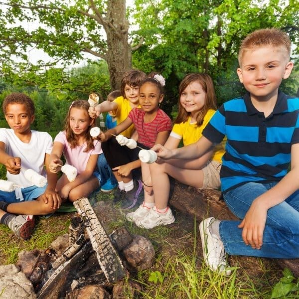 Group of kids sit near bonfire with marshmallow