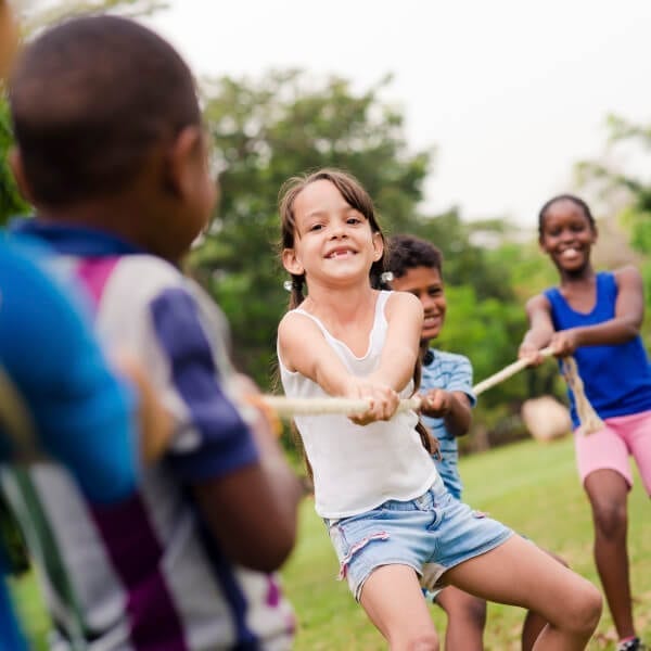 Happy school children playing tug of war with rope in park