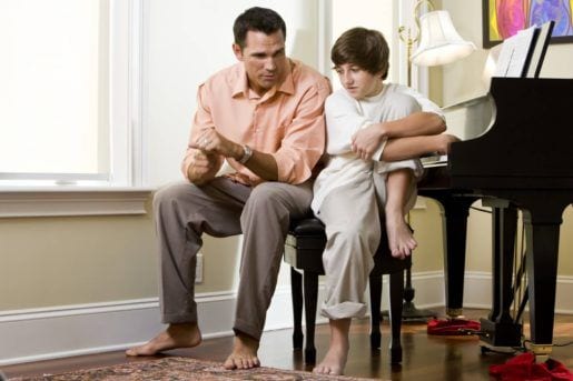 Serious father talking to teenage son at home by piano