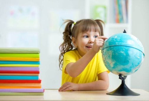 kid girl pointing at globe and sitting at table with books